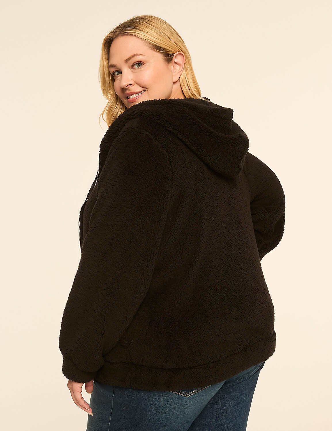 A woman in a black fuzzy jacket and blue jeans smiles over her shoulder against a plain, light-colored background. Product Image 2