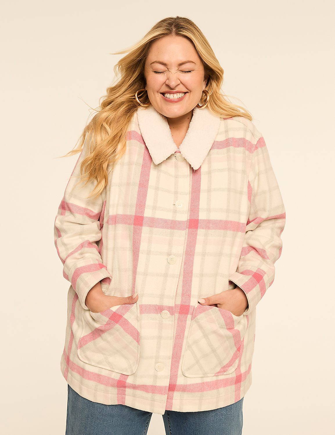 A smiling woman with blonde hair stands with her hands in the pockets of a pink and cream plaid jacket with a sherpa collar, against a plain cream background. Product Image 1