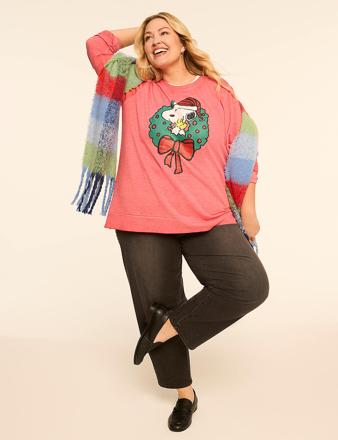 A woman in a festive Snoopy sweatshirt and dark pants poses against a plain, light-colored background, draped in a colorful striped scarf. Product Image 3