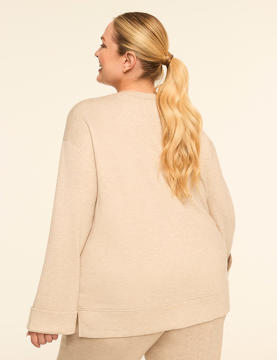 A woman with blonde hair in a ponytail, wearing a beige sweatshirt and pants, stands against a plain beige background. Product Image 2