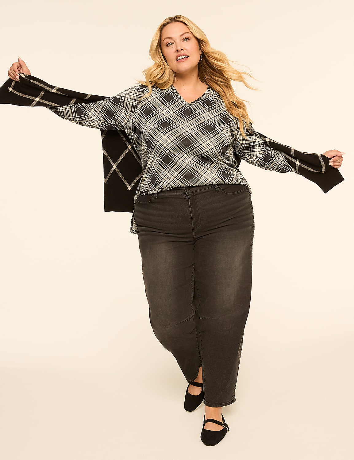 A woman in a plaid sweater and dark jeans poses with her arms outstretched against a plain, light-colored background. Product Image 3