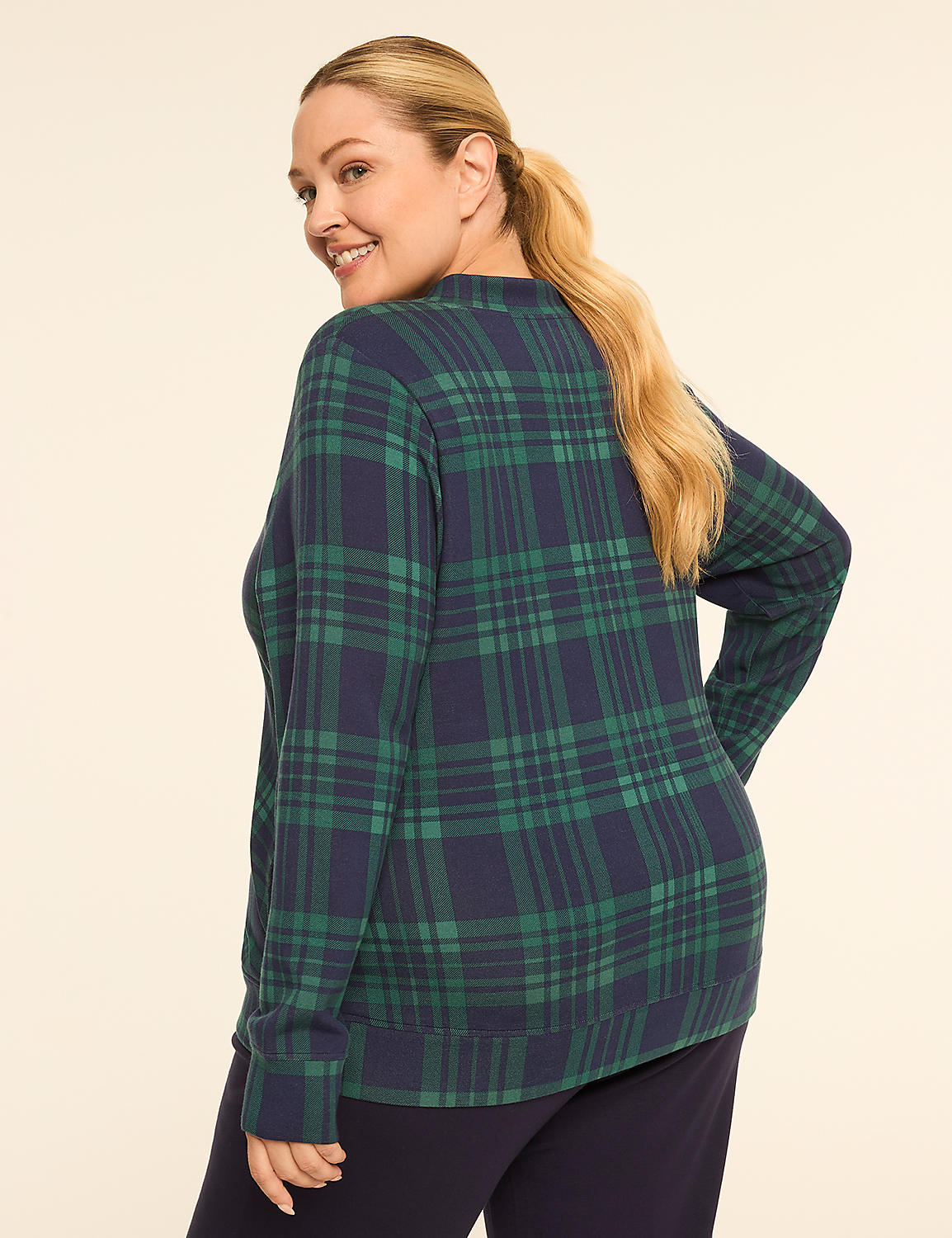 A woman in a green and navy plaid sweater and dark pants smiles over her shoulder against a plain, light background. Product Image 2