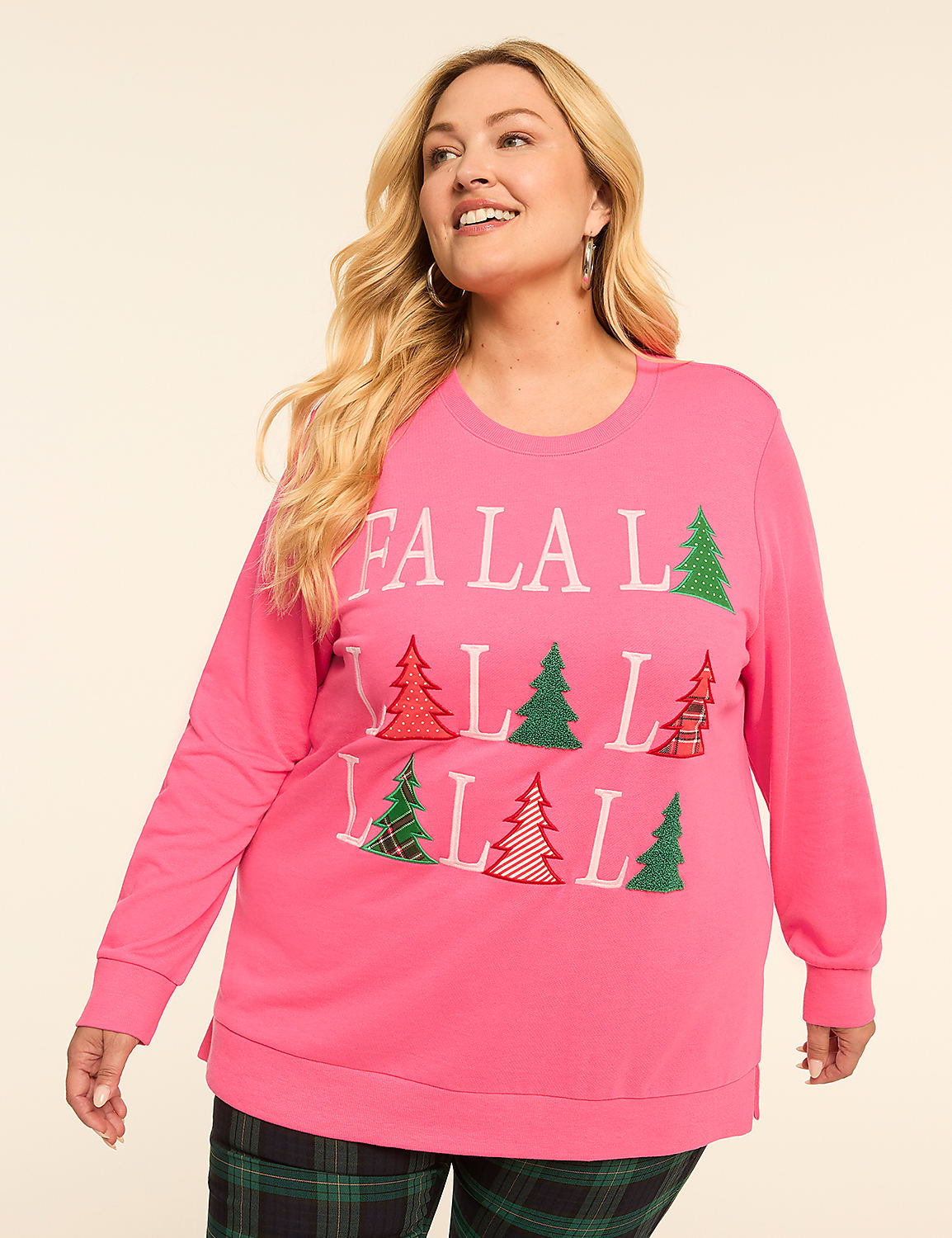 A woman in a pink "Fa La La" Christmas tree sweatshirt stands against a plain background, wearing plaid pants. Product Image 1