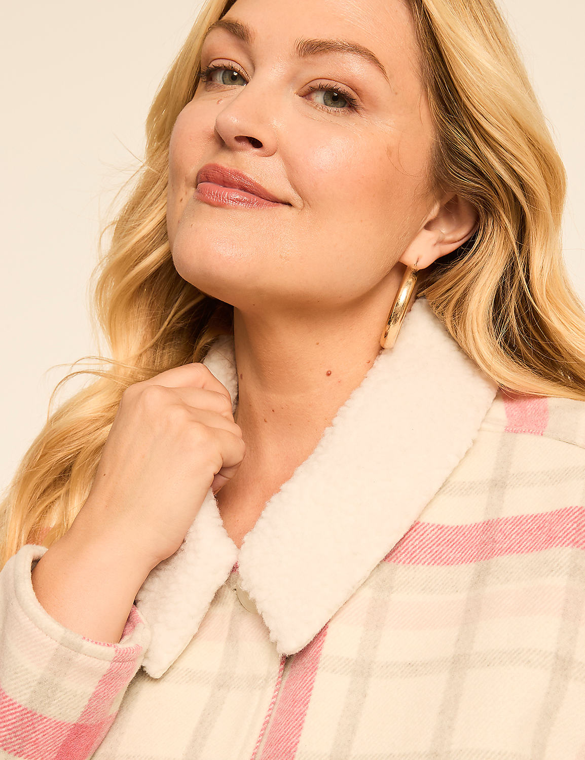 A woman with blonde hair and hoop earrings smiles as she adjusts the collar of her cream and pink plaid jacket against a plain, light background. Product Image 4