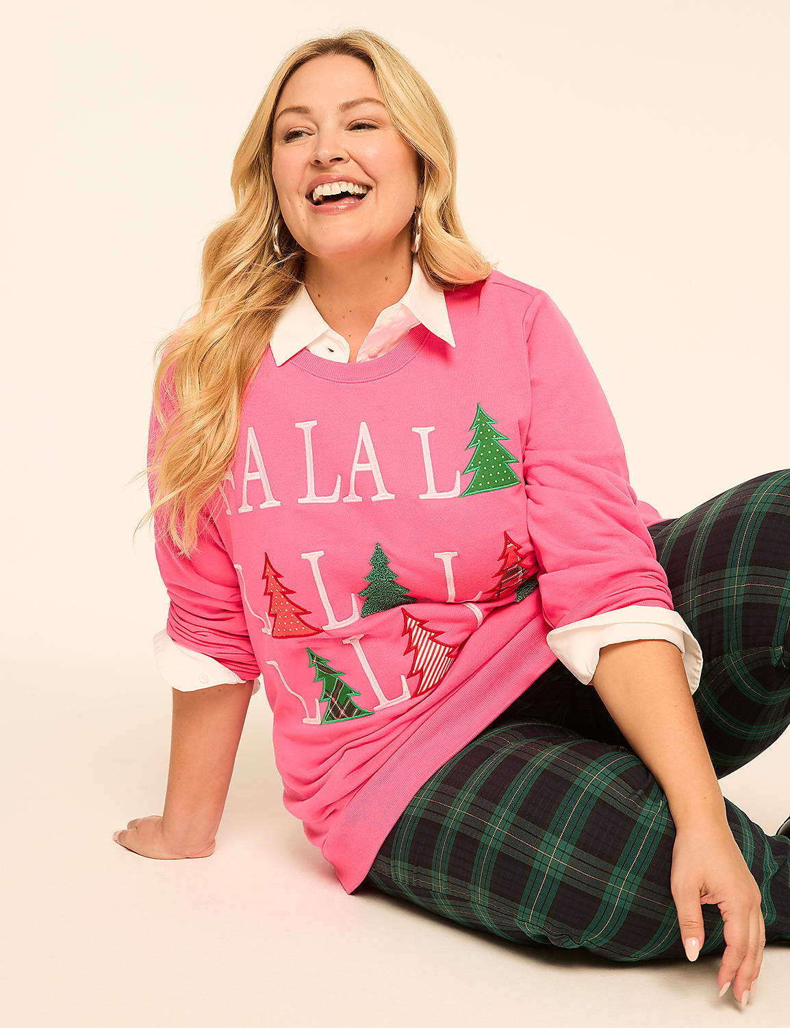 A smiling woman in a pink "LA LA LA" sweatshirt and plaid pants sits on a plain background. Product Image 3