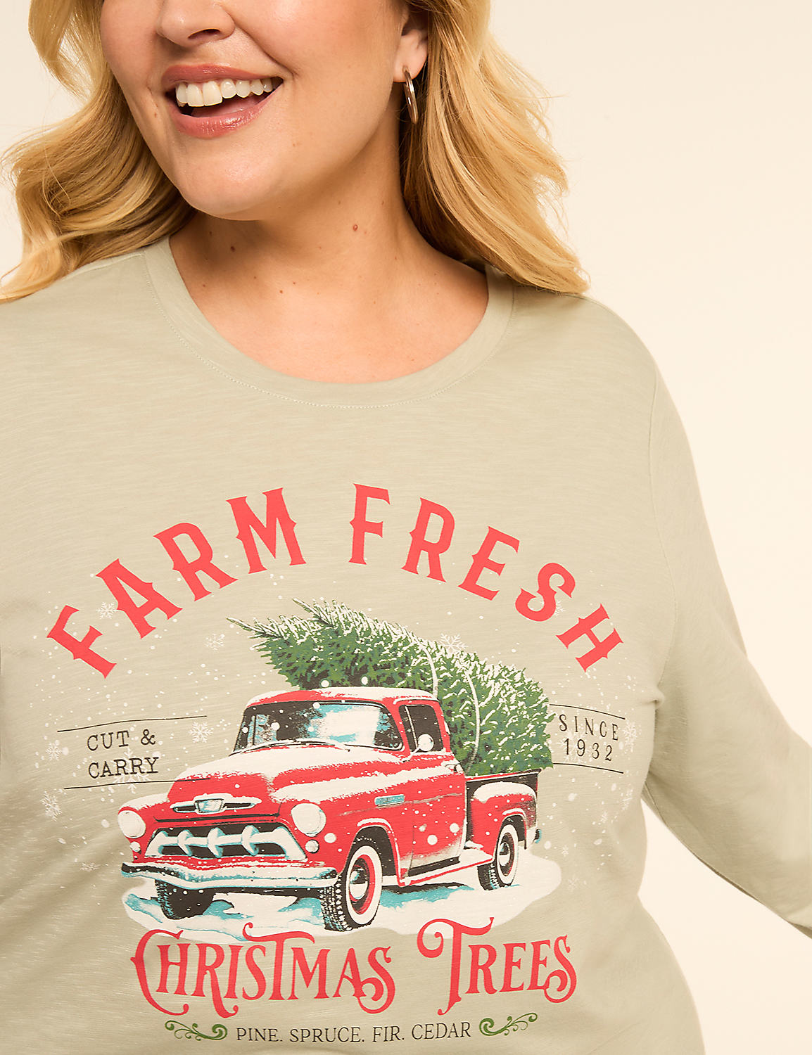 A woman smiles as she wears a light green long-sleeved shirt featuring a vintage red truck loaded with Christmas trees and the words "FARM FRESH CHRISTMAS TREES" printed in red and white against a plain background. Product Image 4