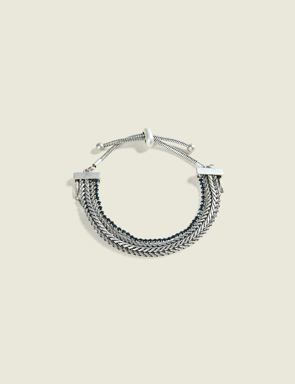 A layered silver chain bracelet with dark beads rests on a pale, textured background. Product Image 1
