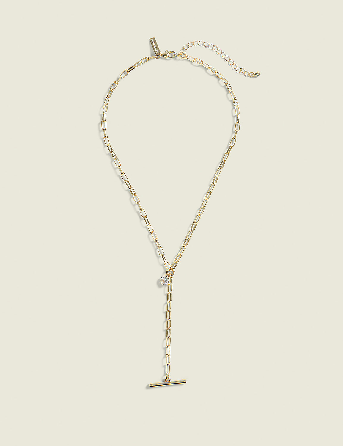 A delicate gold necklace with a toggle clasp and a small charm hangs against a plain, light beige background. Product Image 1