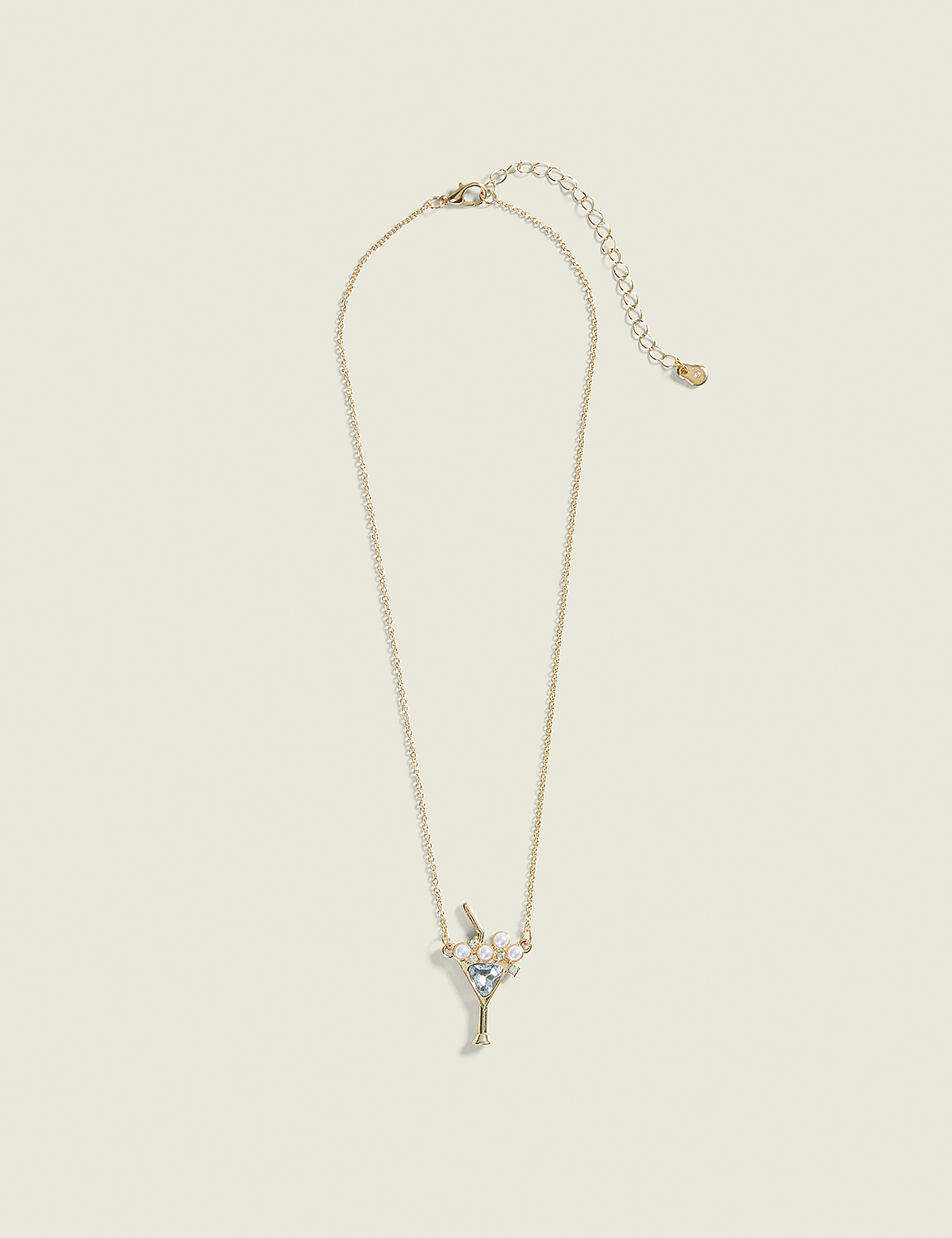 A delicate gold necklace with a martini glass charm adorned with small pearls and blue gems hangs against a plain, light beige background. Product Image 1
