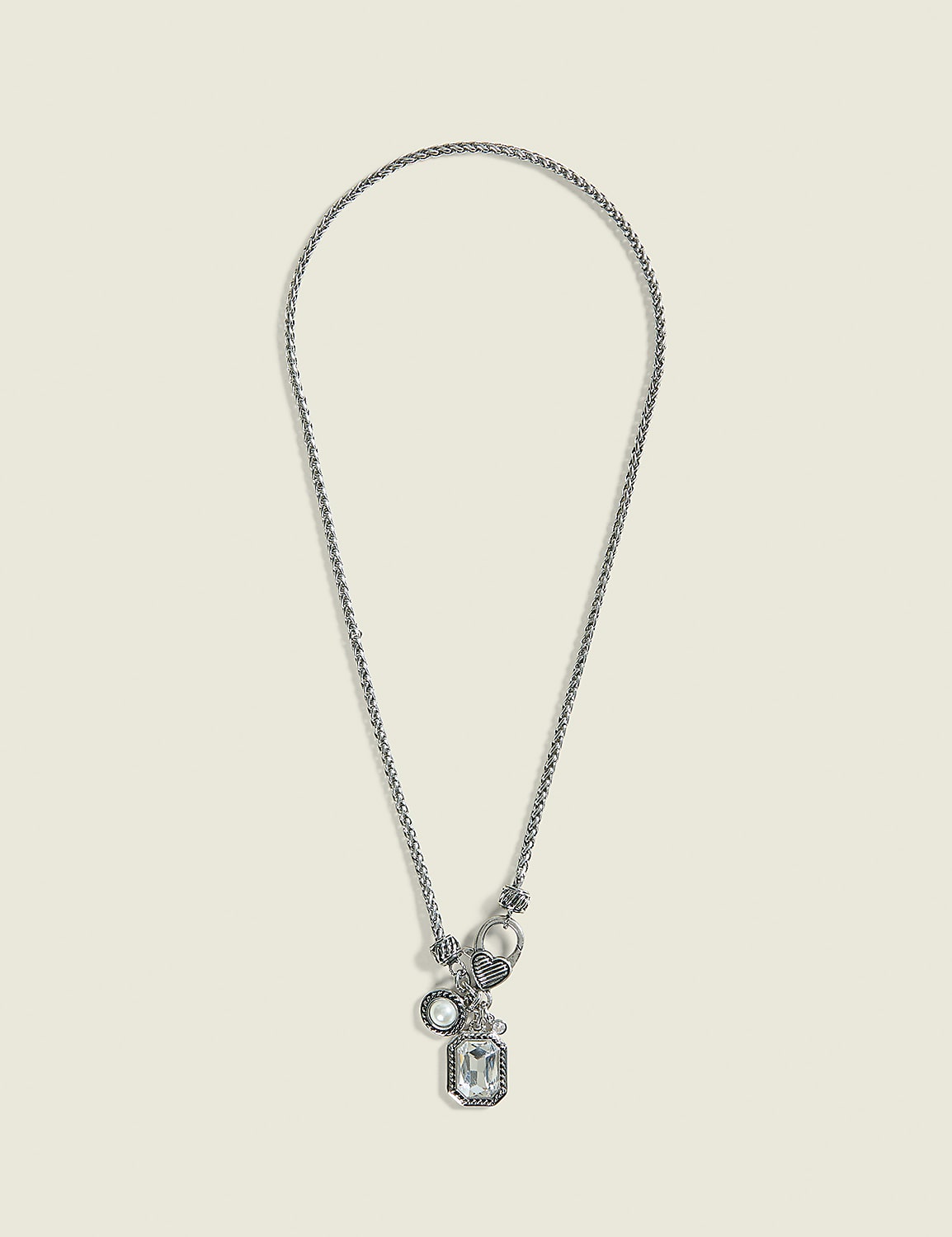 A silver necklace with a rectangular crystal pendant and smaller charms hangs against a plain, light beige background. Product Image 1