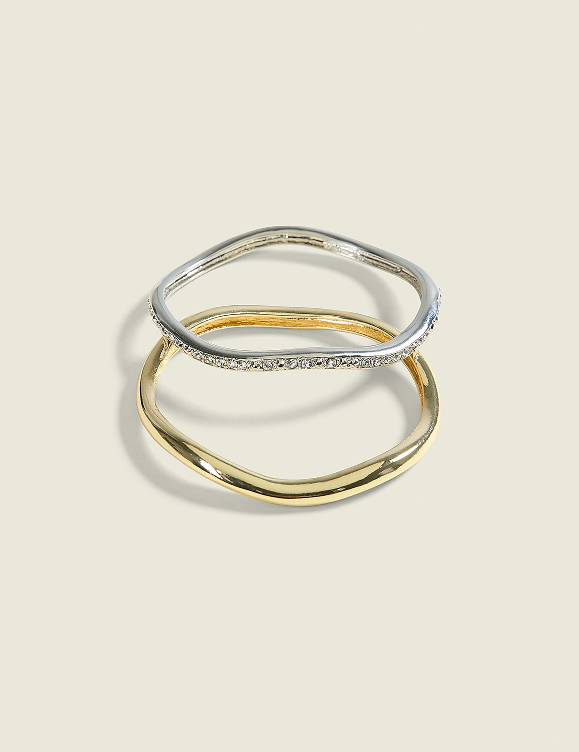 Two wavy rings, one silver with small stones and one gold, are stacked on a pale, textured background. Product Image 1