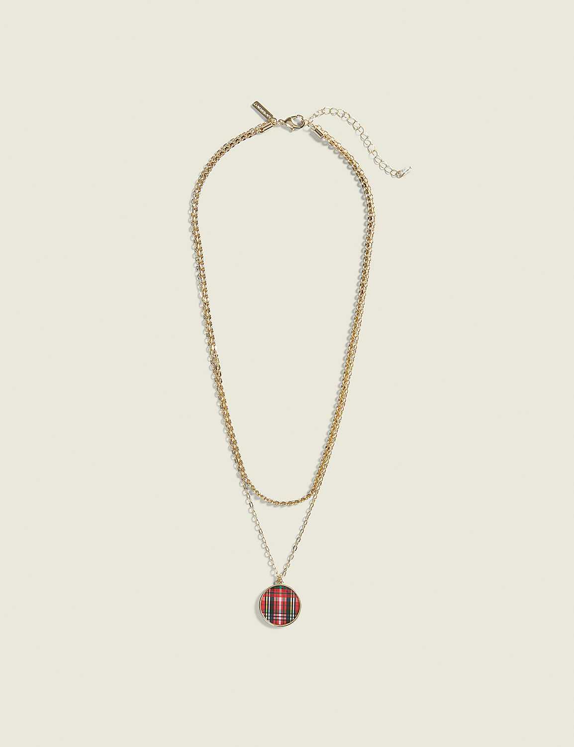 A layered gold necklace with a red and black plaid pendant hangs against a plain, light beige background. Product Image 1
