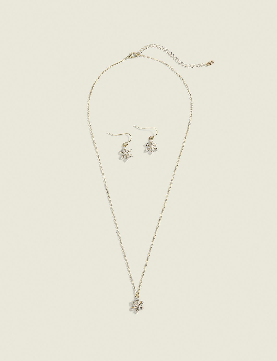 A delicate gold necklace with a snowflake pendant and matching snowflake earrings rest on a plain, light beige background. Product Image 1