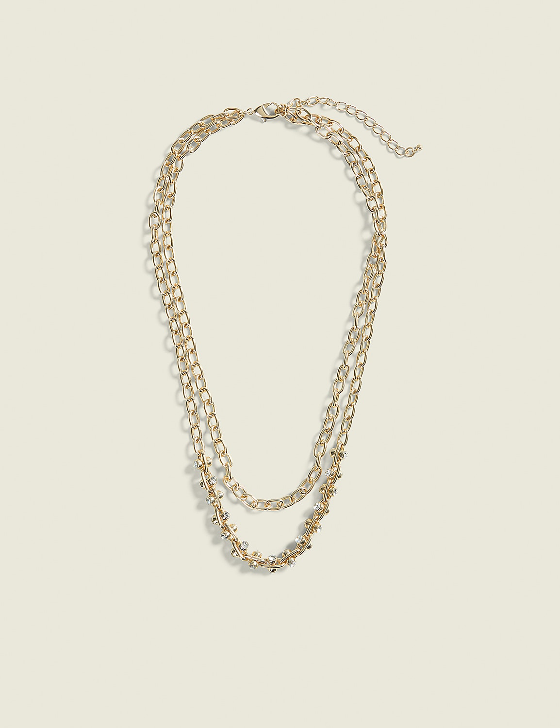 A layered gold chain necklace with small beaded accents rests on a plain, light beige background. Product Image 1