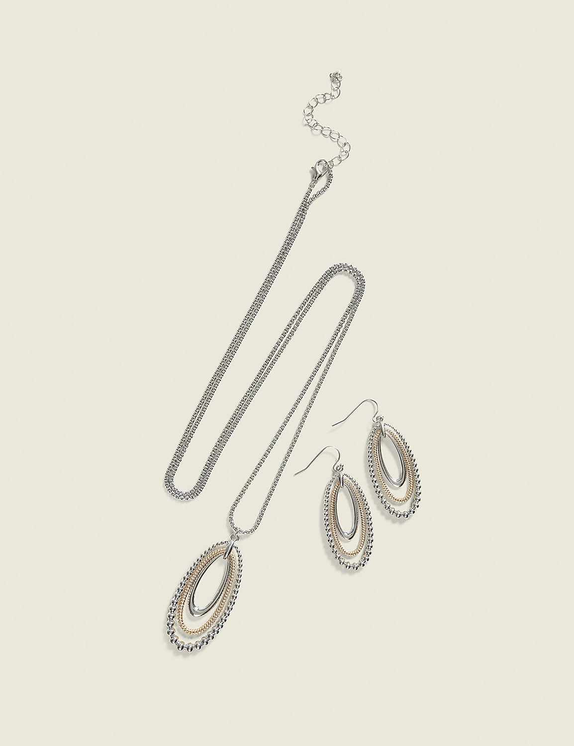 A silver necklace with an oval pendant and matching oval drop earrings are laid out on a plain, light beige background. Product Image 1