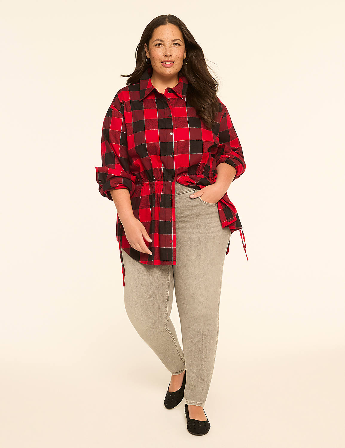 A woman in a red and black plaid shirt and grey jeans stands against a plain, light-colored background. Product Image 3