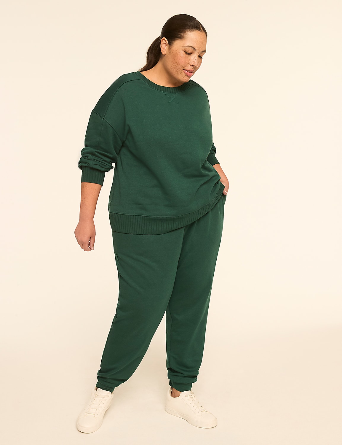 A woman in a green tracksuit stands with her hands in her pockets against a plain, light-colored background. Product Image 3