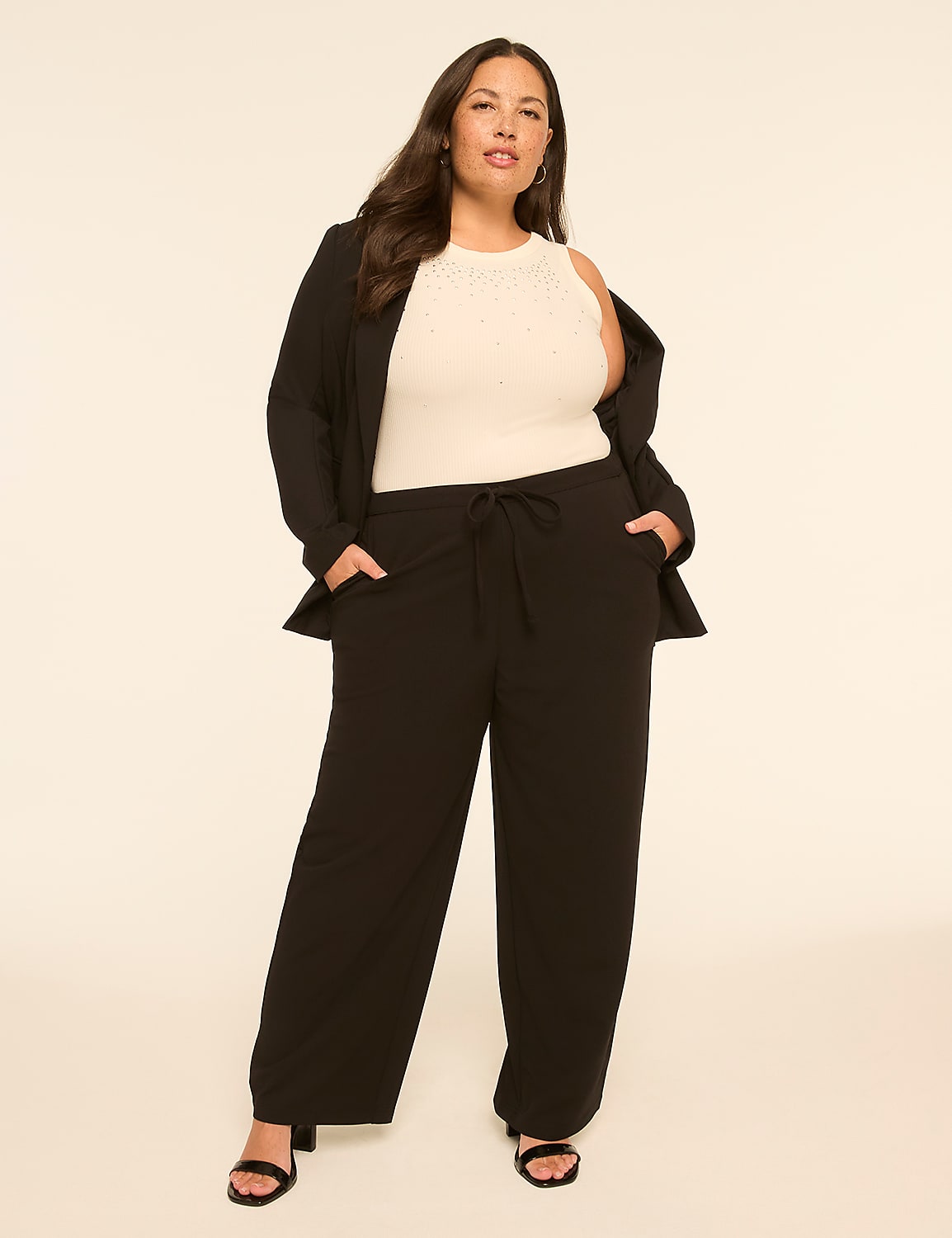 A woman in a white top, black blazer, and black pants stands with her hands in her pockets against a plain, light-colored background. Product Image 3