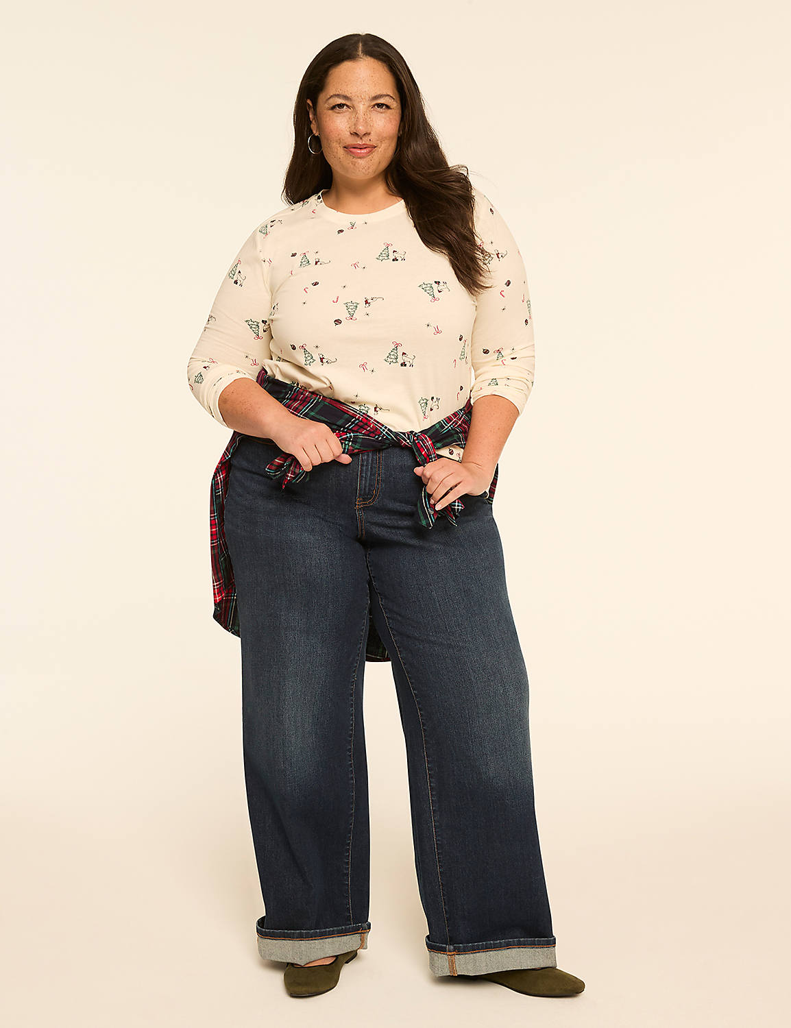 A woman with dark hair stands in the foreground wearing a patterned shirt, dark wide-leg jeans, and a plaid shirt tied around her waist, against a plain, light-colored background. Product Image 3