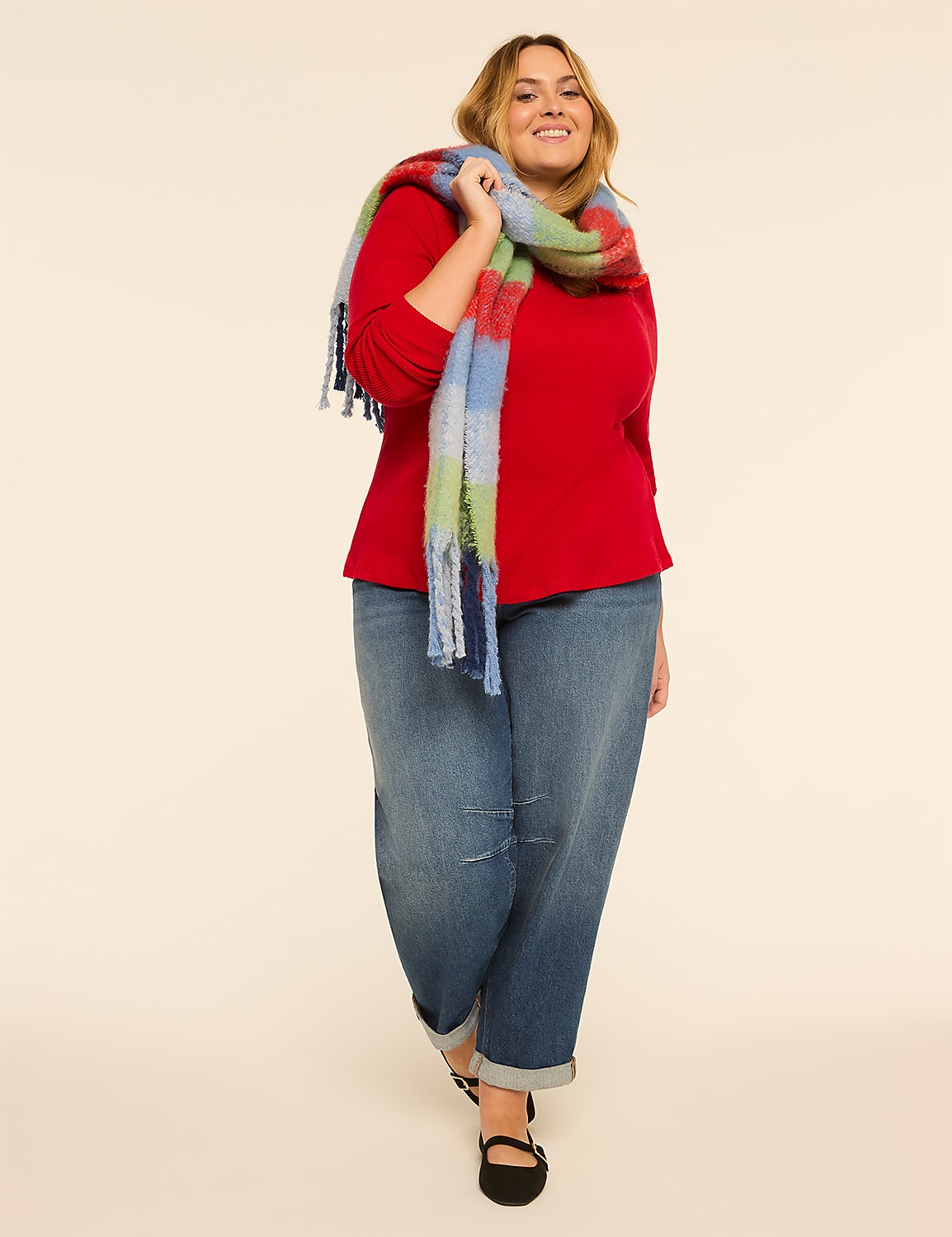 A smiling woman in a red top, blue jeans, and a colorful plaid scarf walks forward against a plain, light-colored background. Product Image 3
