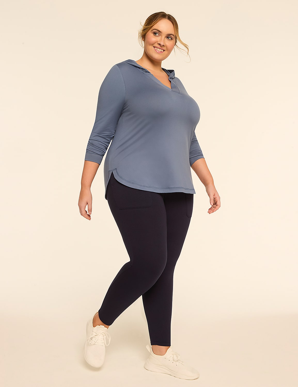 A smiling woman in a blue hooded shirt and dark leggings stands against a plain, light-colored background. Product Image 3
