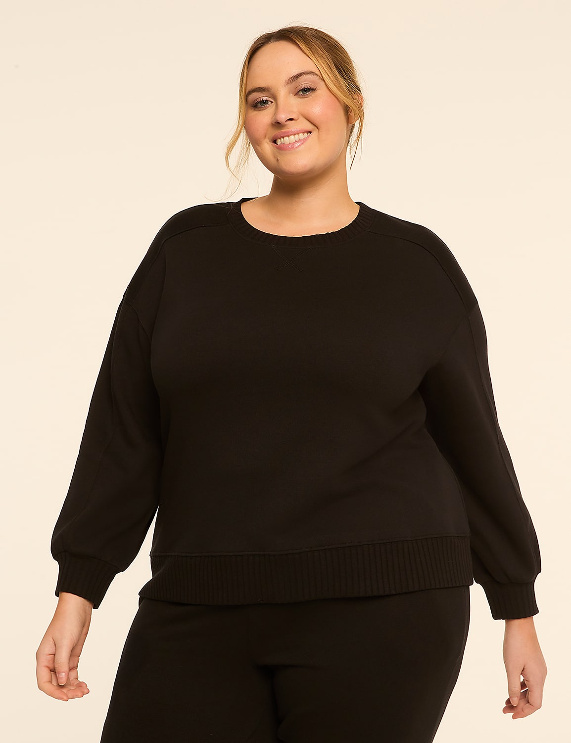 A smiling woman in a black sweater and pants stands against a plain, light-colored background. Product Image 1