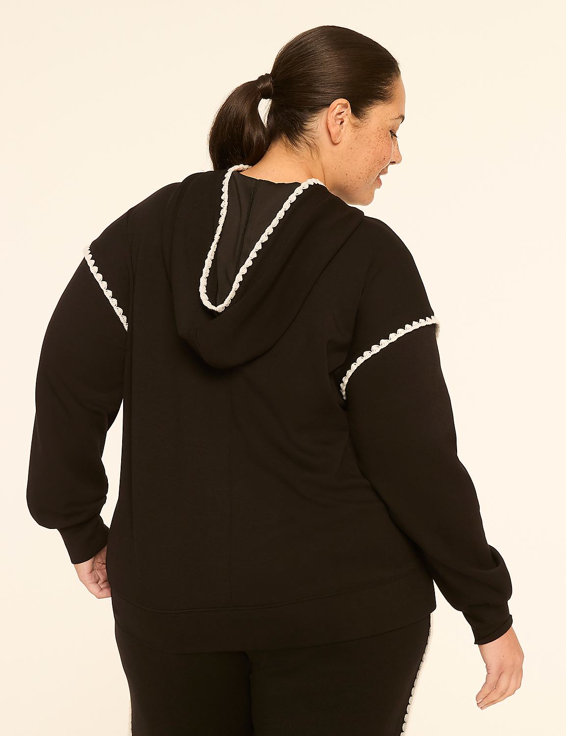A woman in a black hoodie with white trim stands against a plain, light-colored background. Product Image 2