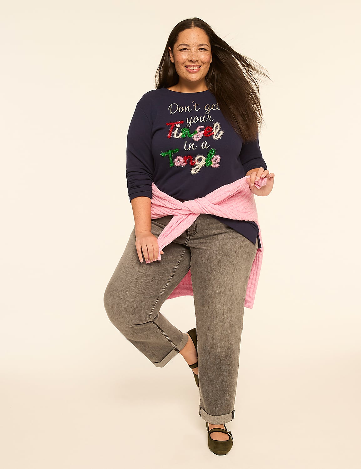A smiling woman in a navy blue holiday-themed shirt and gray jeans stands against a plain, light-colored background. Product Image 3