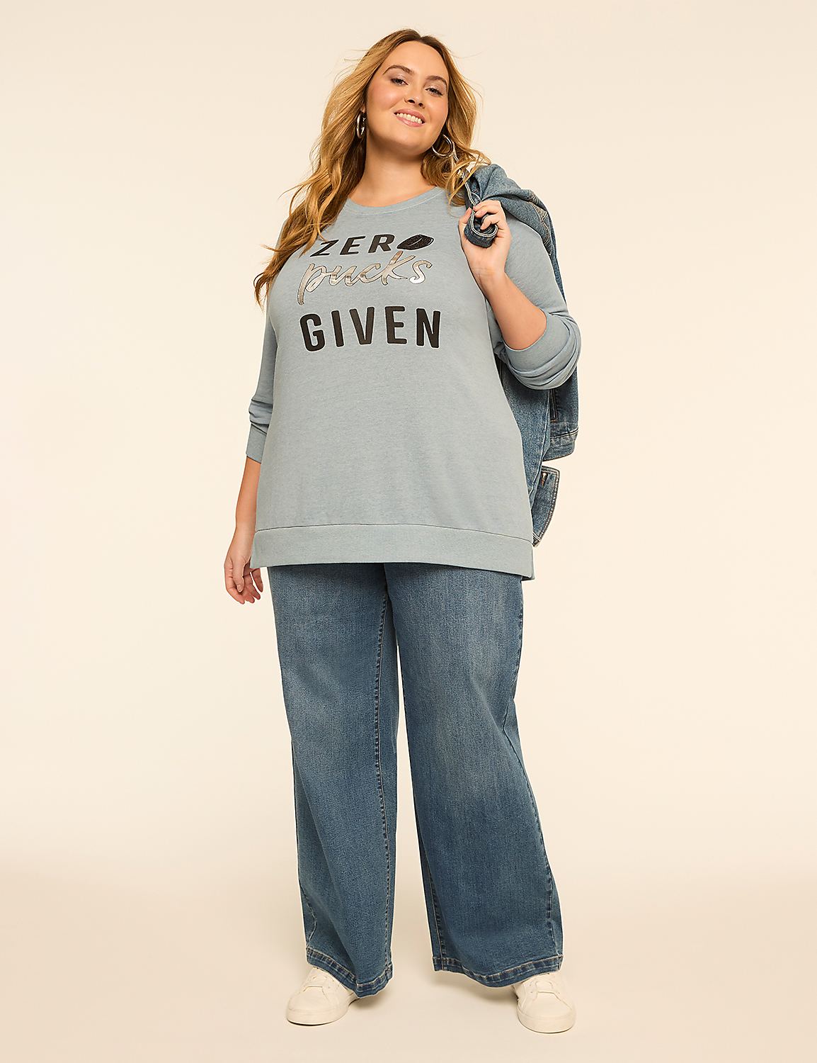A woman in a light blue sweatshirt and wide-leg jeans stands against a plain, light background, with a denim jacket slung over her shoulder. Product Image 3