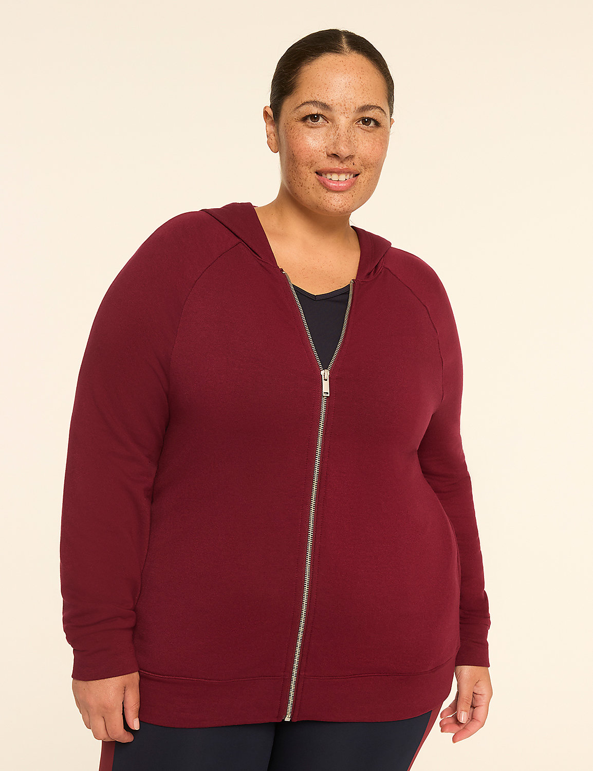 A woman in a maroon zip-up hoodie stands against a plain, light-colored background. Product Image 1