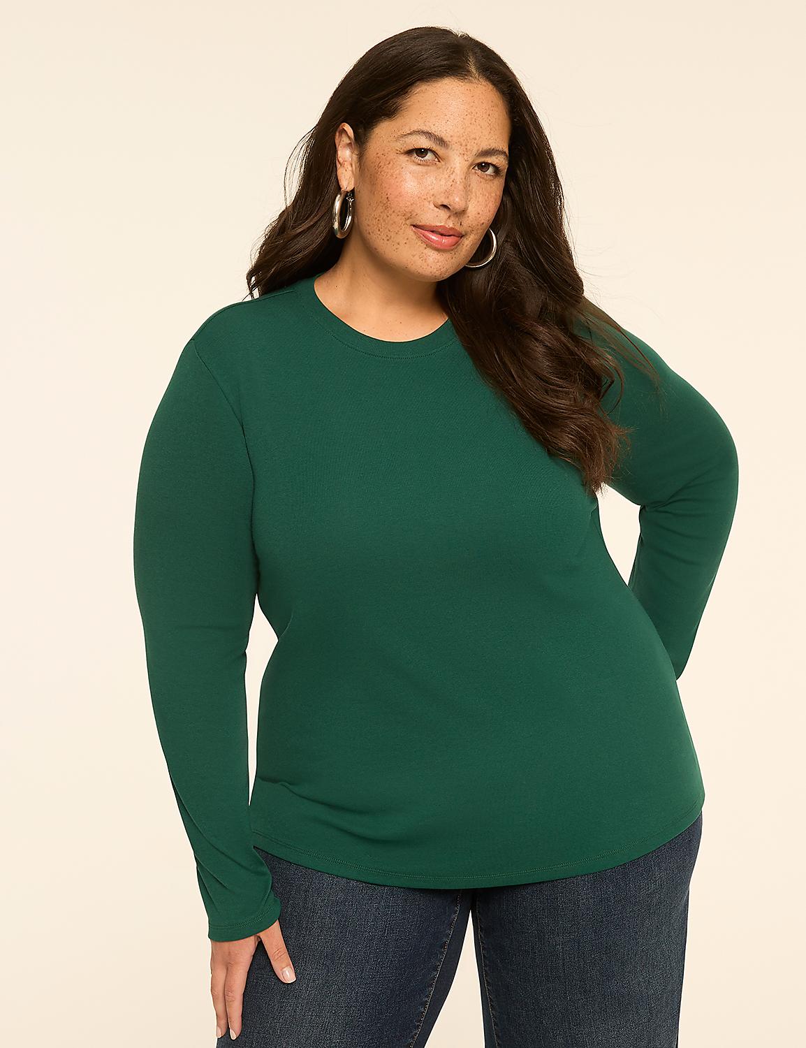 A woman with long, dark hair and hoop earrings stands in the foreground wearing a green long-sleeved shirt and blue jeans, against a plain, light-colored background. Product Image 1