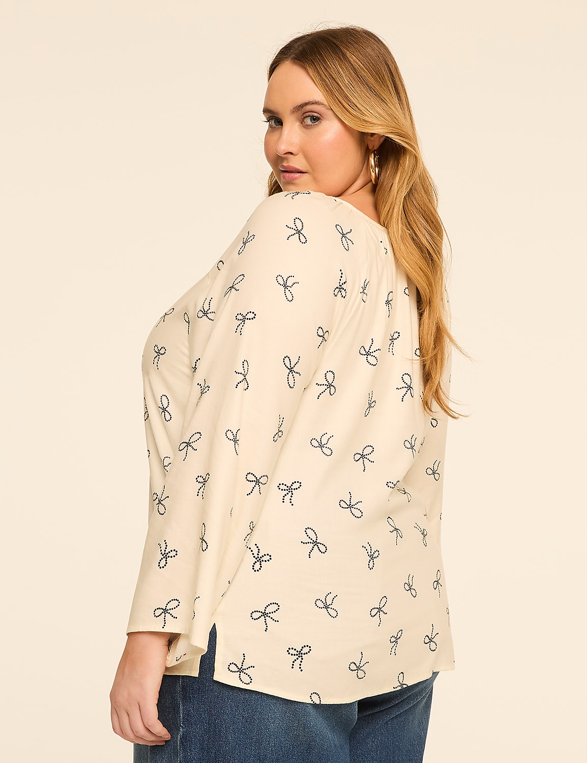 A woman with blonde hair and a cream-colored top with a bow pattern poses against a plain, light background. Product Image 2