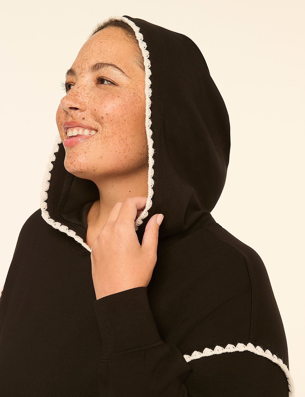 A smiling woman with freckles in a black hoodie with white trim looks to the side against a plain, light-colored background. Product Image 4