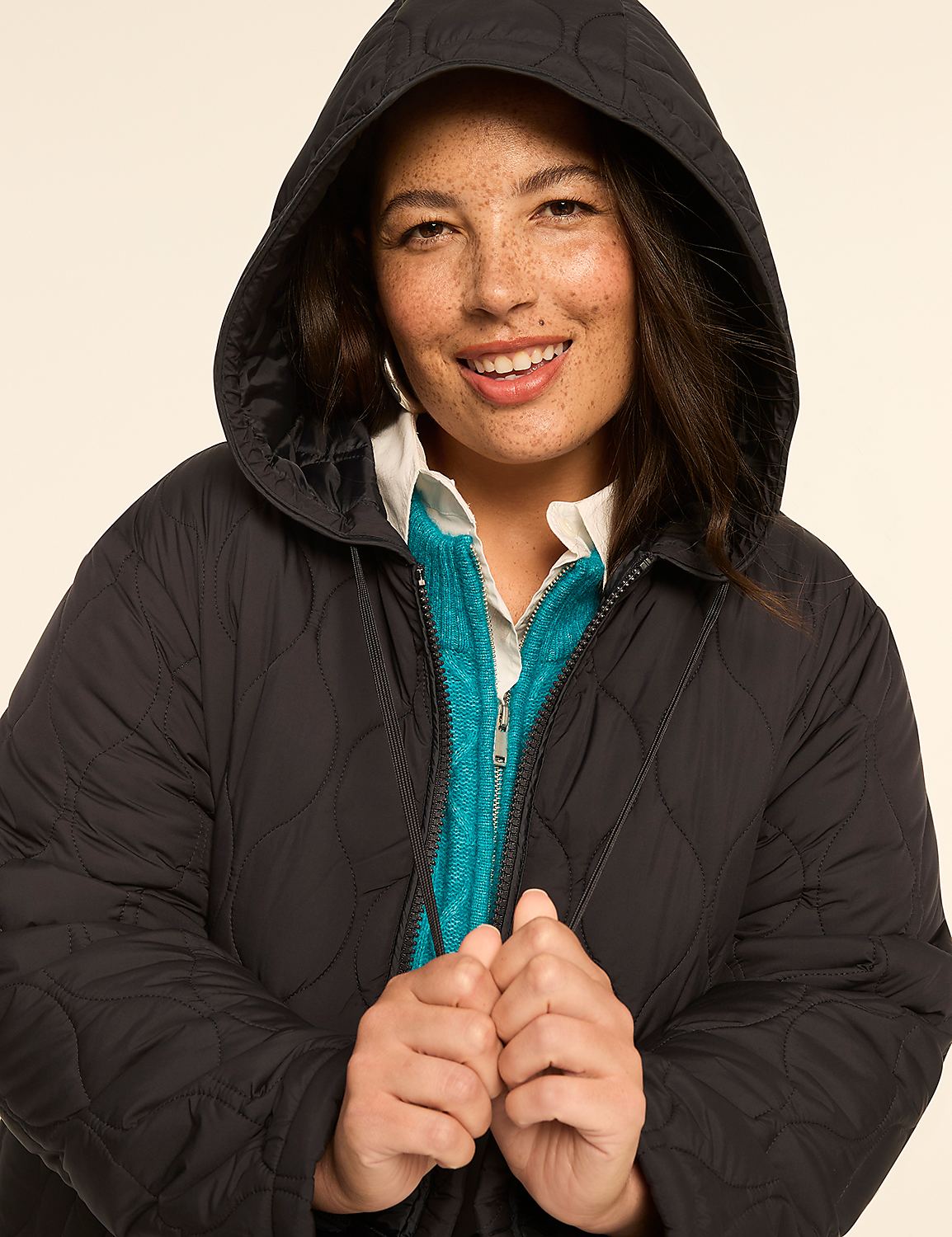 A smiling woman in a quilted black hooded jacket and a teal sweater is centered against a plain, light background. Product Image 4