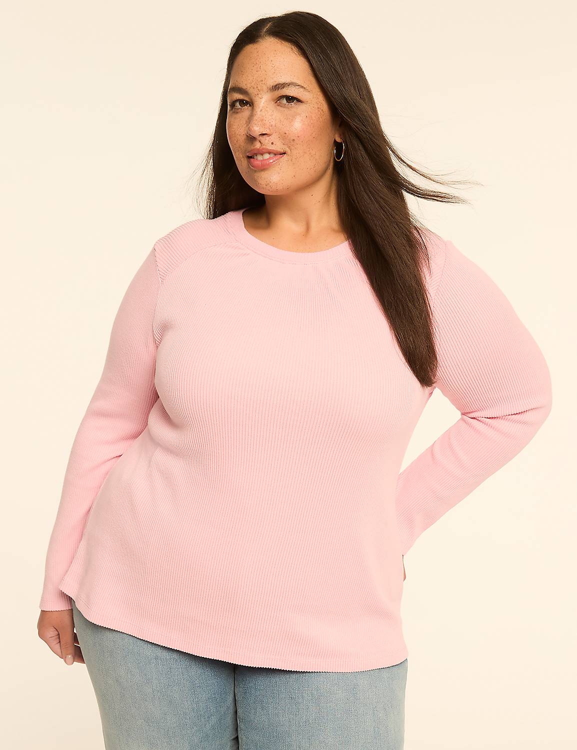 A woman with dark hair and fair skin, wearing a pink waffle-knit top and blue jeans, stands against a plain, light-colored background. Product Image 1
