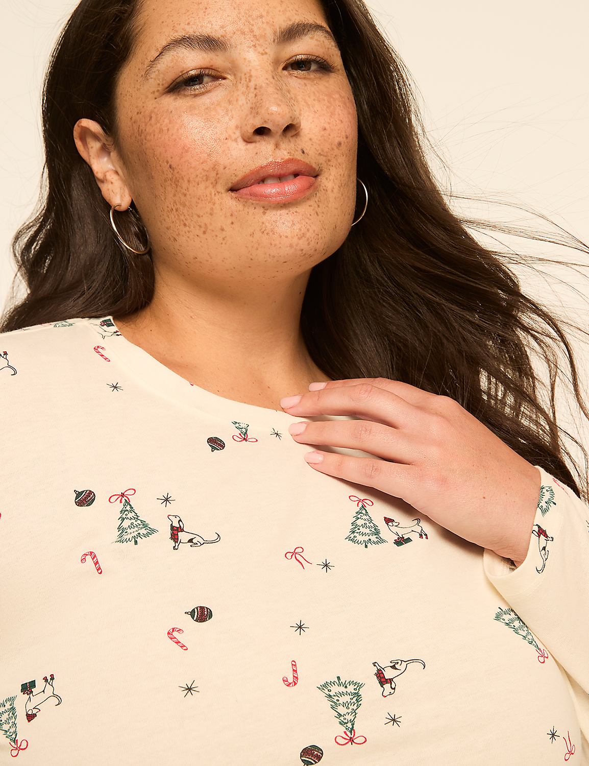 A woman with freckles smiles gently, her cream-colored shirt adorned with a festive Christmas pattern of trees, candy canes, and dogs. Product Image 4