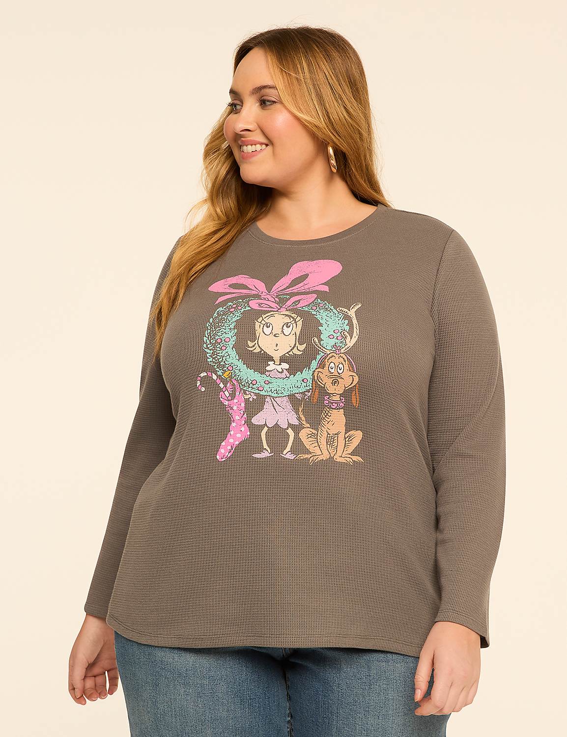 A woman in a grey long-sleeved shirt with a Christmas-themed graphic of Cindy Lou Who and Max the dog stands against a plain beige background. Product Image 1