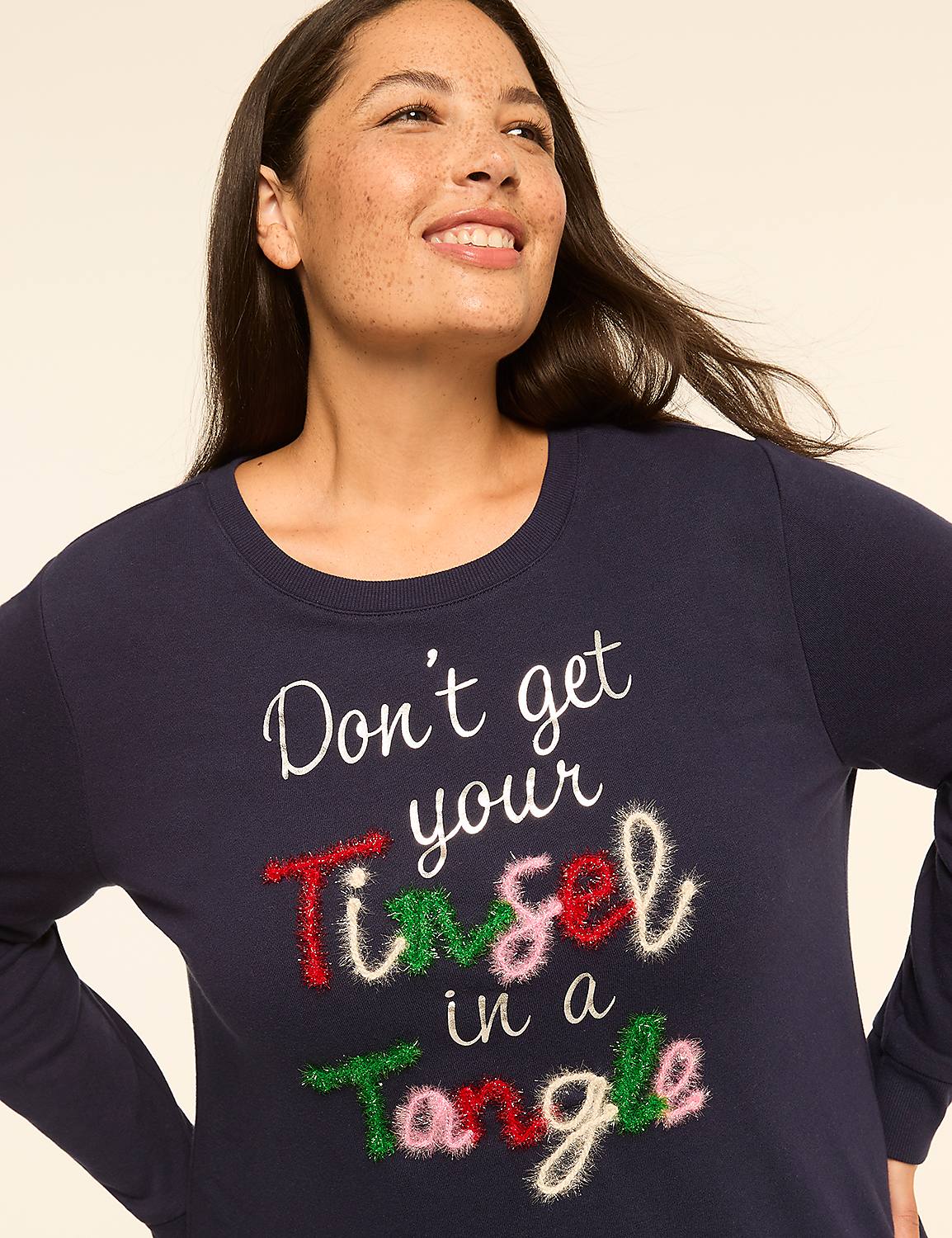 A smiling woman in a navy blue long-sleeved shirt with a festive holiday slogan stands against a plain, light-colored background. Product Image 4