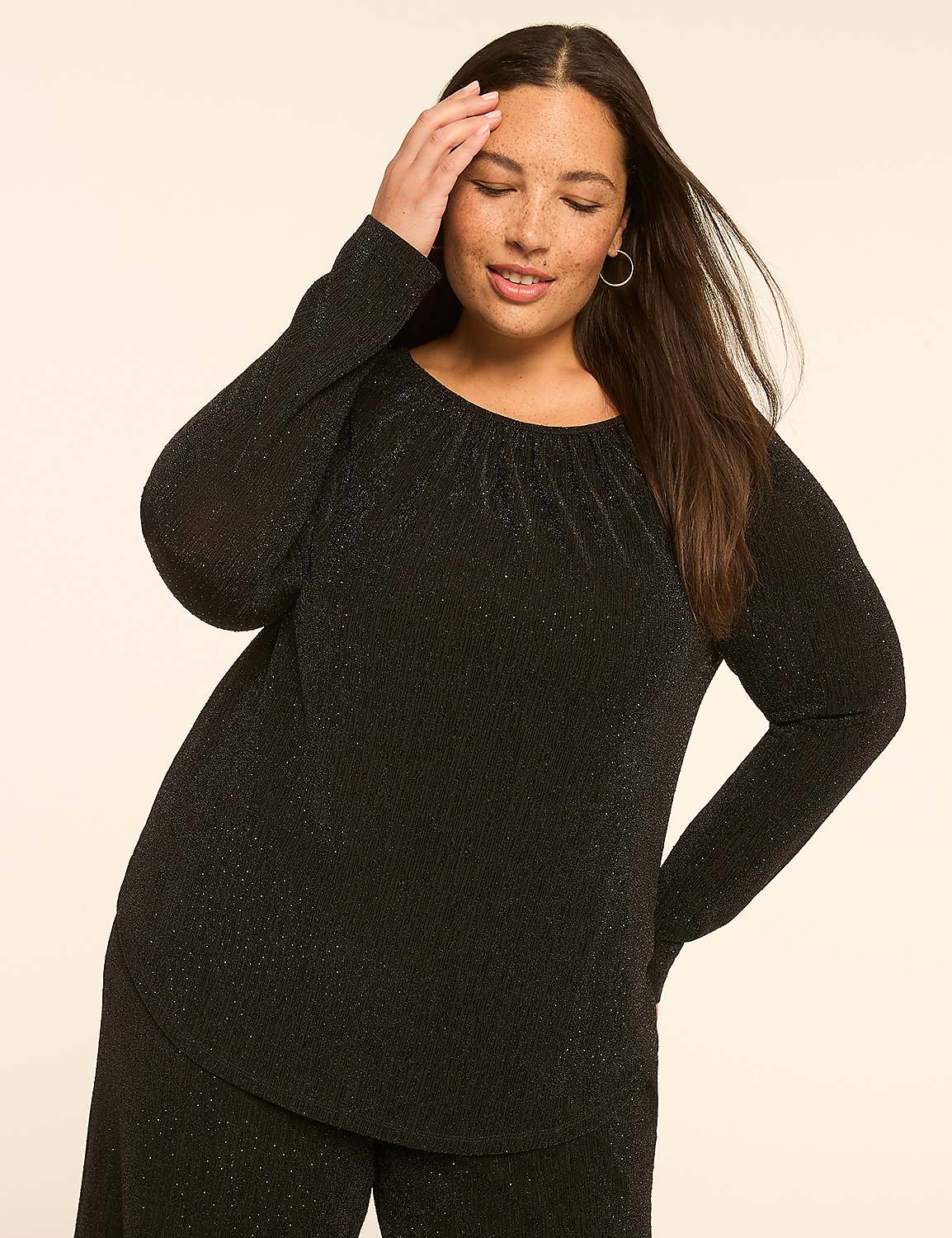 A woman in a black sparkly top and pants poses with her hand on her head against a plain beige background. Product Image 1