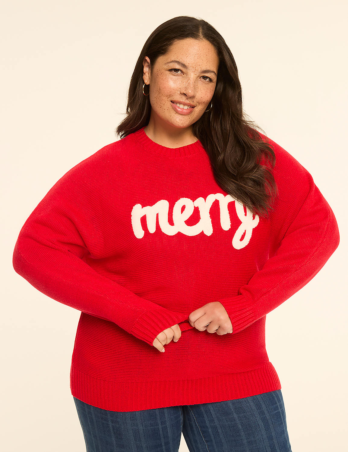 A woman in a red "merry" sweater stands against a plain, light-colored background. Product Image 1