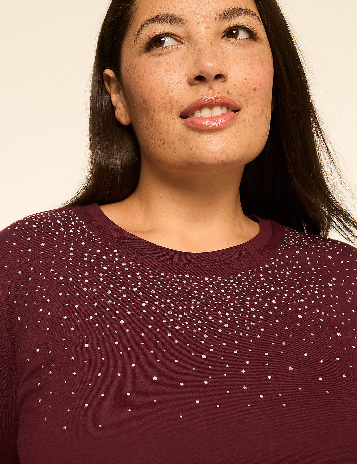 A woman with freckles smiles softly, her burgundy sweater adorned with scattered rhinestones against a plain, light background. Product Image 4