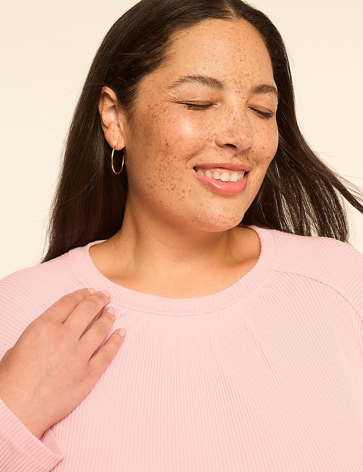A smiling woman with freckles and closed eyes wears a pink sweater in the foreground, against a plain, light-colored background. Product Image 4