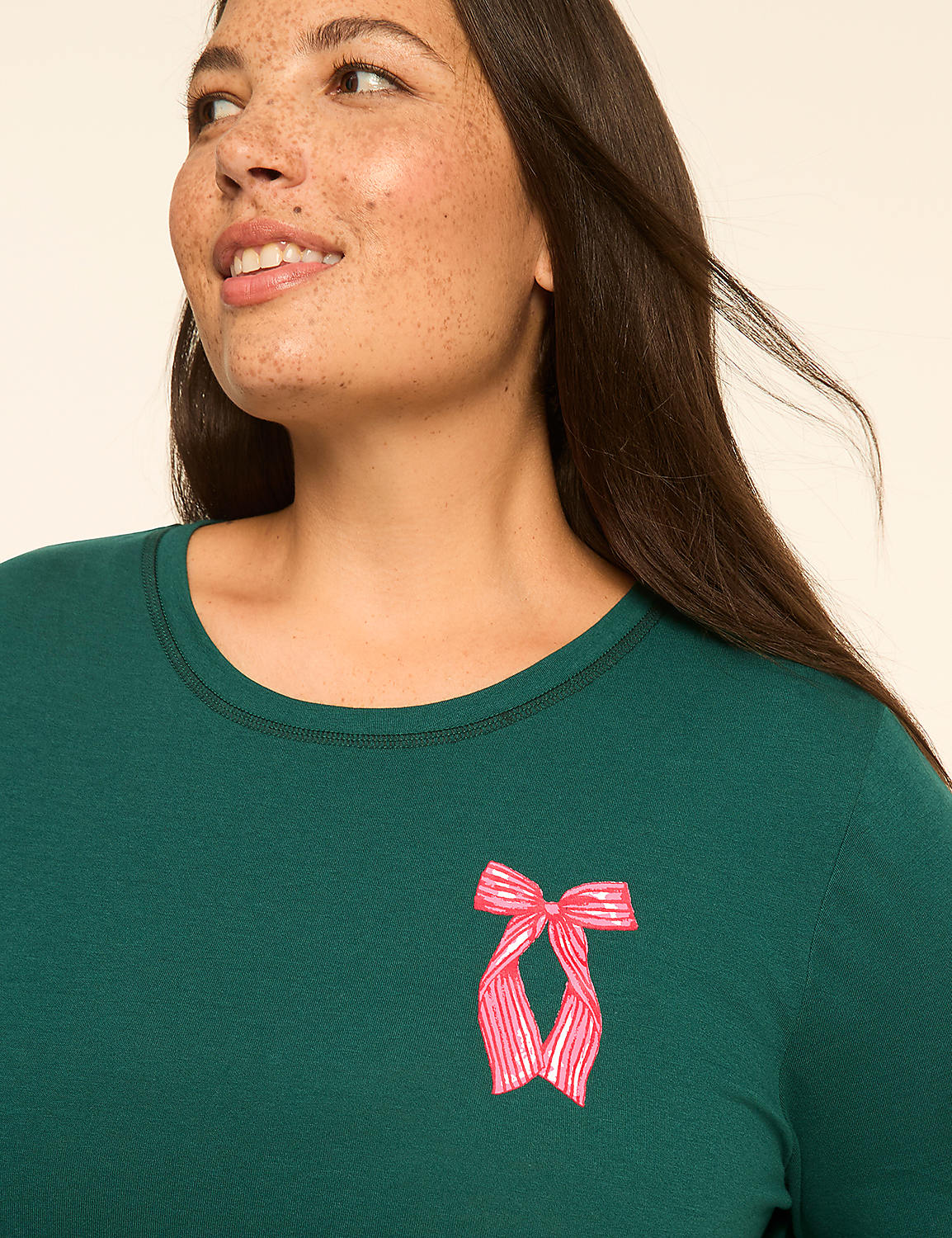 A woman with freckles smiles as she looks to the side, wearing a dark green shirt with a pink bow on the chest, against a plain, light background. Product Image 3