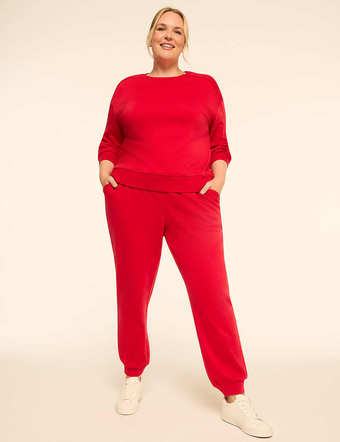 A smiling woman in a red tracksuit stands with her hands in her pockets against a plain, light-colored background. Product Image 3