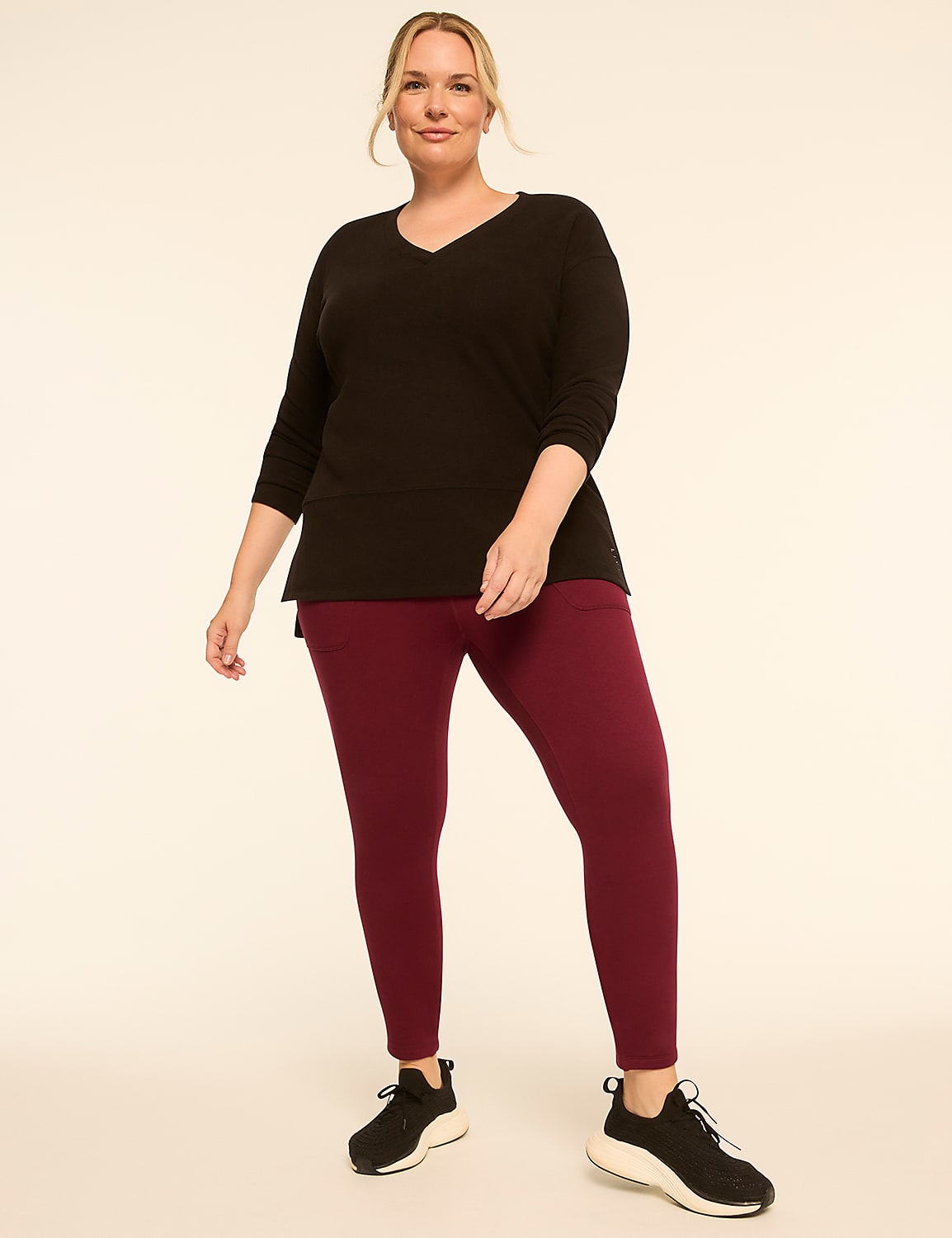 A woman in a black v-neck shirt and burgundy leggings stands against a plain, light-colored background. Product Image 3