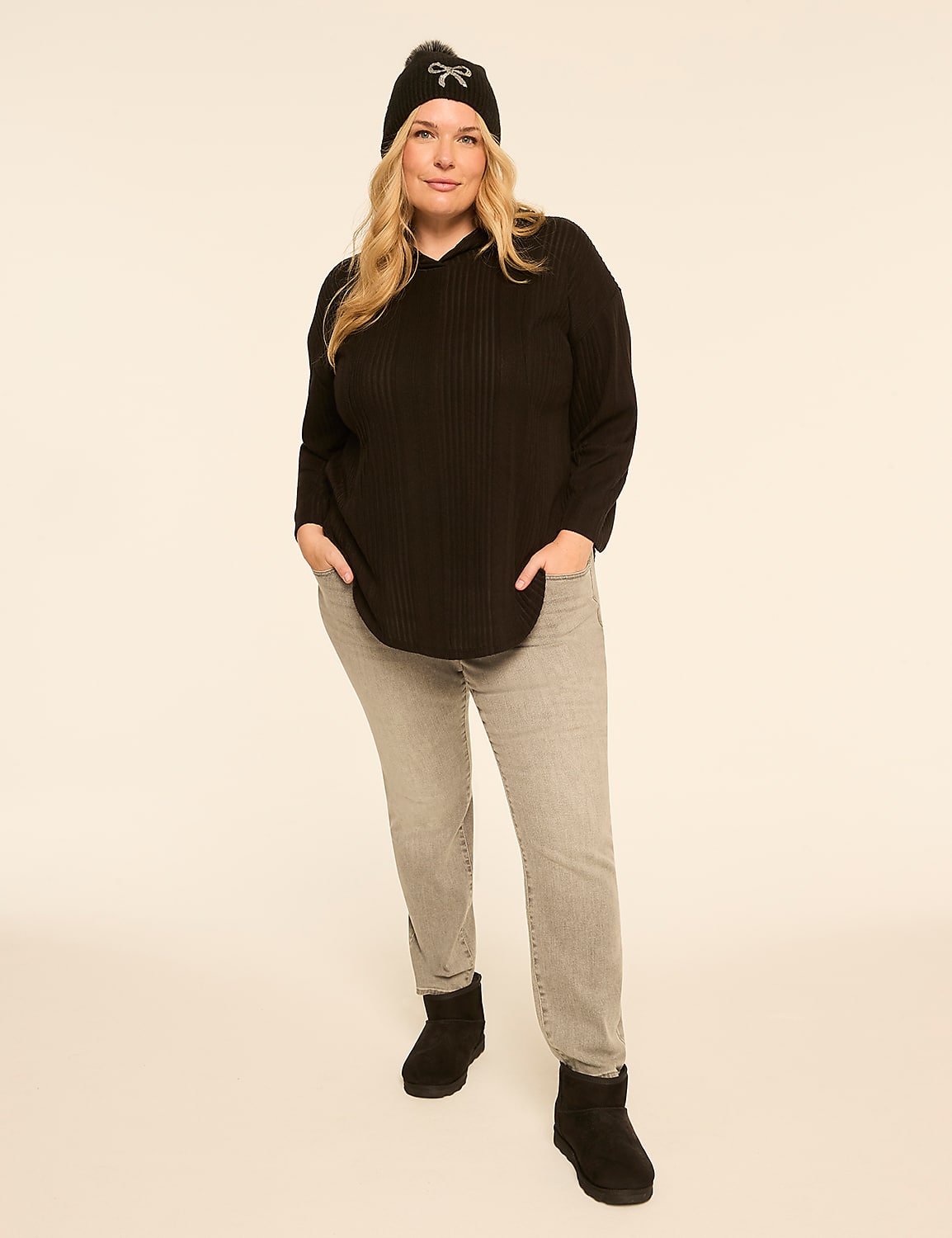 A woman in a black beanie, black top, and grey jeans stands against a plain, light-colored background. Product Image 3