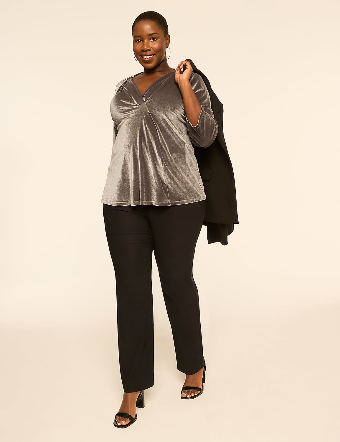 A smiling woman in a gray velvet top and black pants stands against a plain, light-colored background, with a black blazer draped over her shoulder. Product Image 3