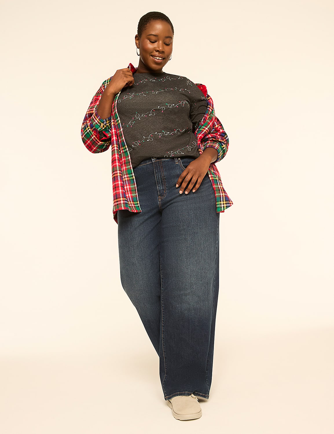 A woman in a dark patterned sweater, open plaid shirt, and wide-leg jeans stands against a plain, light-colored background. Product Image 3
