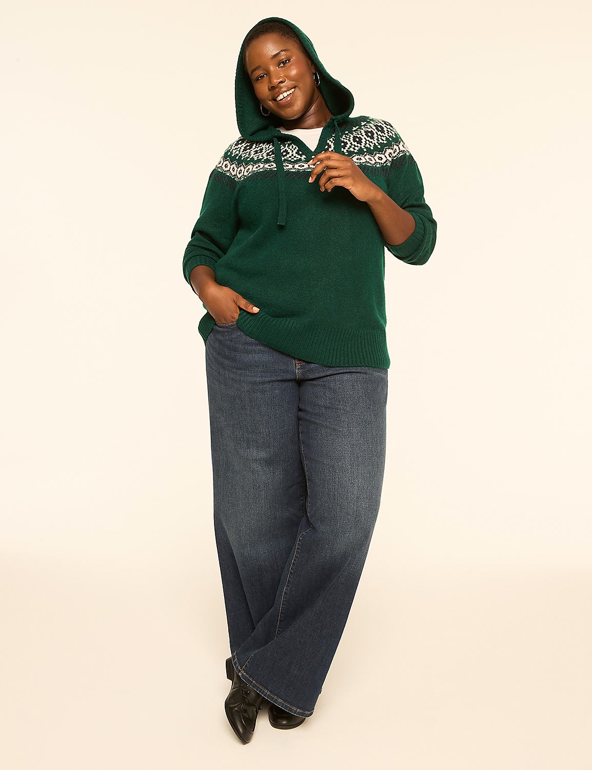 A smiling woman in a green hooded sweater and wide-leg jeans stands against a plain, light-colored background. Product Image 3