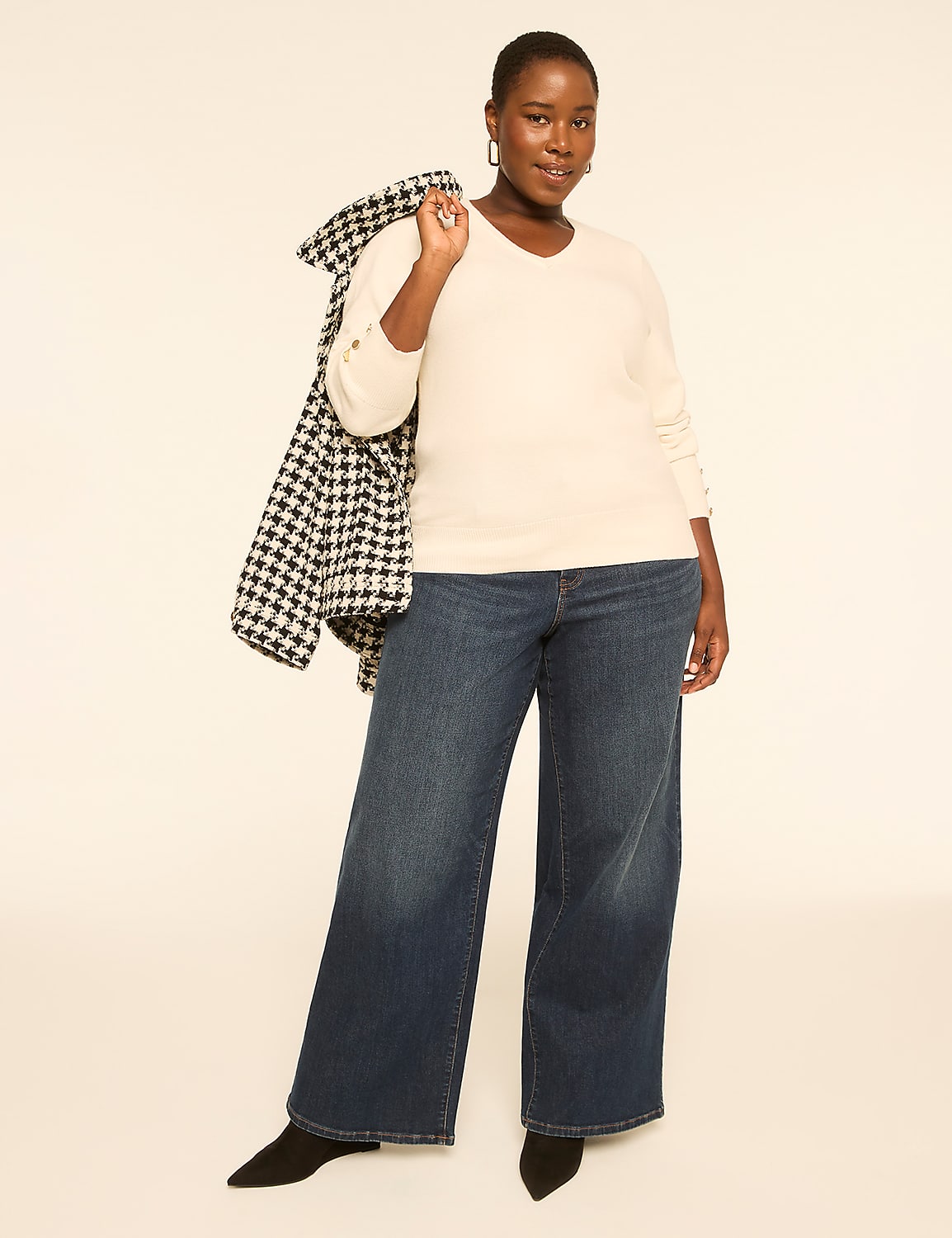 A woman in a cream sweater and wide-leg jeans stands against a plain, light-colored background, with a houndstooth coat draped over her shoulder. Product Image 3